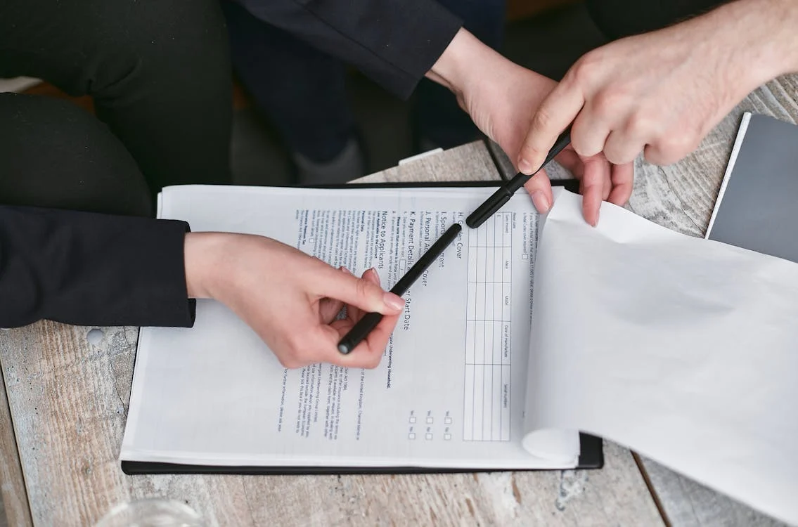 person being instructed by another person to sign papers with a black pen