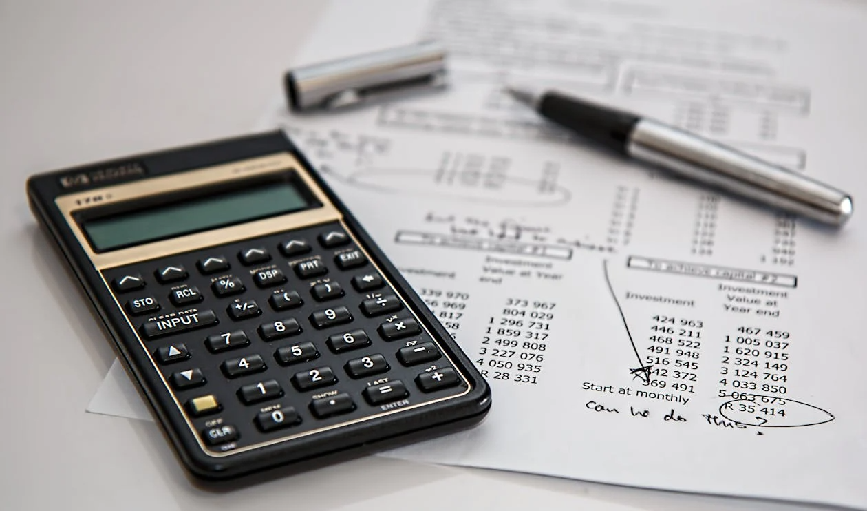 Calculator and pen placed on a financial report with handwritten notes and figures.