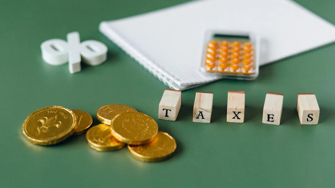 Taxes written using wooden blocks next to gold coins