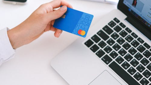 An image of a person holding a credit card while working on a laptop