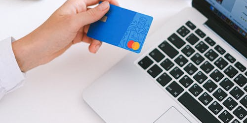 An image of a person holding a credit card while working on a laptop